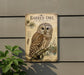 a vintage-style metal sign with an illustration of a barred owl perched on a branch, surrounded by pine needles and berries.