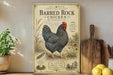 a vintage-style metal sign with an illustration of a black and white chicken, placed on a wooden shelf next to a wooden cutting board and some potted plants.