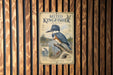 A vintage-style poster of a belted kingfisher, a type of bird, is displayed on a wooden wall.