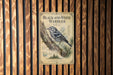 A vintage-style metal sign with a black and white illustration of a bird perched on a tree branch, mounted on a wooden wall.