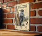 A metal sign with an illustration of a black-backed woodpecker on a brick wall.