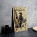 a metal sign with an illustration of a black-backed woodpecker, along with text and a map, placed on a table next to some black camera lenses.