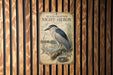 a poster of a black-crowned night-heron, which is a type of wading bird, displayed on a wooden wall.