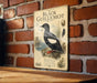 a vintage-style metal sign with an illustration of a black guillemot perched on a rock, mounted on a brick wall.