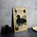 A metal sign with illustrations and text about the Black Scoter bird, placed on a table next to some black camera lenses.