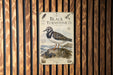 a vintage-style poster or sign with a black and white illustration of a bird, likely a sandpiper, perched on a rock. The poster is mounted on a wooden wall with vertical slats.