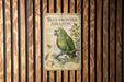A vintage-style metal sign with a colorful illustration of a parrot, mounted on a wooden wall.