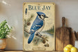 A vintage-style poster of a blue jay is displayed on a shelf, accompanied by a potted plant, a wooden cutting board, and some lemons.