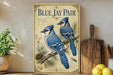 A vintage-style poster featuring two blue jays perched on a branch, with pine cones and other natural elements, is displayed on a shelf next to a wooden cutting board and some lemons.