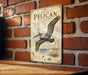 A vintage-style metal sign with an illustration of a pelican in flight, mounted on a brick wall.