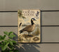 a vintage-style metal sign with a depiction of a Canadian goose, surrounded by various natural elements such as pine trees, grass, and a bird's nest.