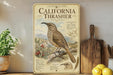 a vintage-style poster of a California thrush, a bird species native to the state, displayed on a shelf alongside a wooden cutting board and some lemons.