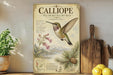 a vintage-style poster of a Callihorn Hummingbird, with a detailed illustration of the bird in flight and various plant life surrounding it. The poster is displayed on a wooden shelf, with a potted plant and a wooden cutting board visible in the background.