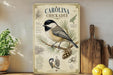 A vintage-style metal sign featuring illustrations and text about the Carolina Chickadee, a small bird with a black cap and gray body, perched on a pine branch.