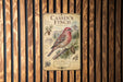 a vintage-style metal sign with a bird illustration, hanging on a wooden wall.