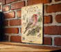 a vintage-style metal sign with a bird illustration, hanging on a brick wall.