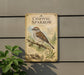 a sign with a detailed illustration of a sparrow perched on a branch, surrounded by various plant life.