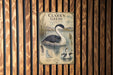 A vintage-style metal sign with a black and white illustration of a bird, likely a duck, in a body of water, mounted on a wooden wall.