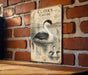 A vintage-style illustration of a bird, likely a waterfowl, is displayed on a brick wall.
