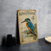 a metal sign with a detailed illustration of a kingfisher bird, accompanied by text that describes the bird's features and habitat.
