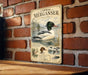 A vintage metal sign featuring a duck illustration and text, mounted on a brick wall.
