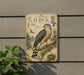 a vintage-style metal sign with a detailed illustration of a hawk perched on a branch, surrounded by pine cones and pine needles.