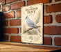 a vintage-style sign with a detailed illustration of a diamond dove perched on a branch, mounted on a brick wall.