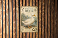 a vintage-style metal sign with an illustration of a duck, placed on a wooden wall.