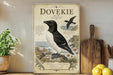 a vintage-style poster or sign with a black and white illustration of a bird, likely a seagull, perched on a rock. The bird is surrounded by various natural elements, such as flowers and plants, creating a serene and coastal atmosphere. The poster is displayed on a shelf or counter, with a potted plant and a wooden cutting board visible in the background.