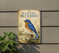 a vintage-style metal sign with a blue and orange bird illustration, mounted on a wall next to a plant.