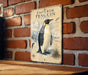 A vintage poster of an Emperor penguin is displayed on a brick wall, featuring an illustration of the penguin and various text elements.