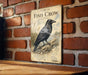 a vintage-style metal sign with a black crow illustration, mounted on a brick wall.