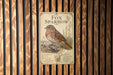 a metal sign with a detailed illustration of a fox sparrow, mounted on a wooden wall.