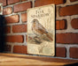 a vintage-style sign with a detailed illustration of a brown and white bird, likely a sparrow, perched on a branch. The sign is mounted on a brick wall and is positioned on a wooden surface.