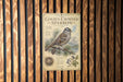 A vintage-style metal sign with an illustration of a golden-crowned sparrow, mounted on a wooden wall.