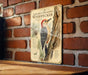 A vintage-style metal sign featuring an illustration of a golden-fronted woodpecker perched on a tree trunk, with text describing the bird.