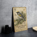 A vintage-style metal sign featuring a detailed illustration of a golden-winged warbler perched on a branch, surrounded by pine cones and other natural elements.
