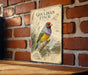a vintage-style metal sign with a colorful illustration of a Gouldian finch, mounted on a brick wall.