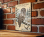 a metal sign with an illustration of a great gray owl in a snowy forest setting.