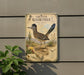 a metal sign with a painting of a roadrunner, mounted on a wall next to a plant.