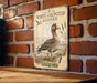 A vintage-style metal sign featuring an illustration of a white-fronted goose, mounted on a brick wall.