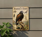 A vintage-style metal sign depicting a Harris's Hawk, a bird of prey, perched on a tree stump with a desert landscape in the background.