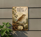 a vintage-style metal plaque with a detailed illustration of a bird perched on a branch, surrounded by plants and flowers.