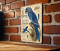 a vintage-style metal sign with a blue parrot illustration, mounted on a brick wall.
