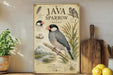 a poster or painting of a Java Sparrow, a small bird with a black and white coloration, perched on a branch. The poster includes illustrations and text that provide information about the bird, such as its size, habitat, and behavior. The poster is displayed on a shelf next to a wooden cutting board and a potted plant, creating a homely and nature-inspired setting.