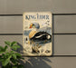 A metal sign with a detailed illustration of a king eider, a large sea bird, is mounted on a wall.