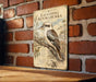 a vintage-style metal sign with a picture of a laughing kookaburra, a type of bird, mounted on a brick wall.