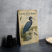 a vintage-style metal sign with illustrations and text, depicting a blue heron standing in a pond.