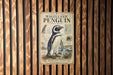 a vintage-style poster of a Magellanic penguin, mounted on a wooden wall.