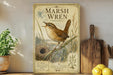 A vintage-style metal plaque featuring an illustration of a marsh wren perched on a branch, with a birdhouse and other natural elements in the background.